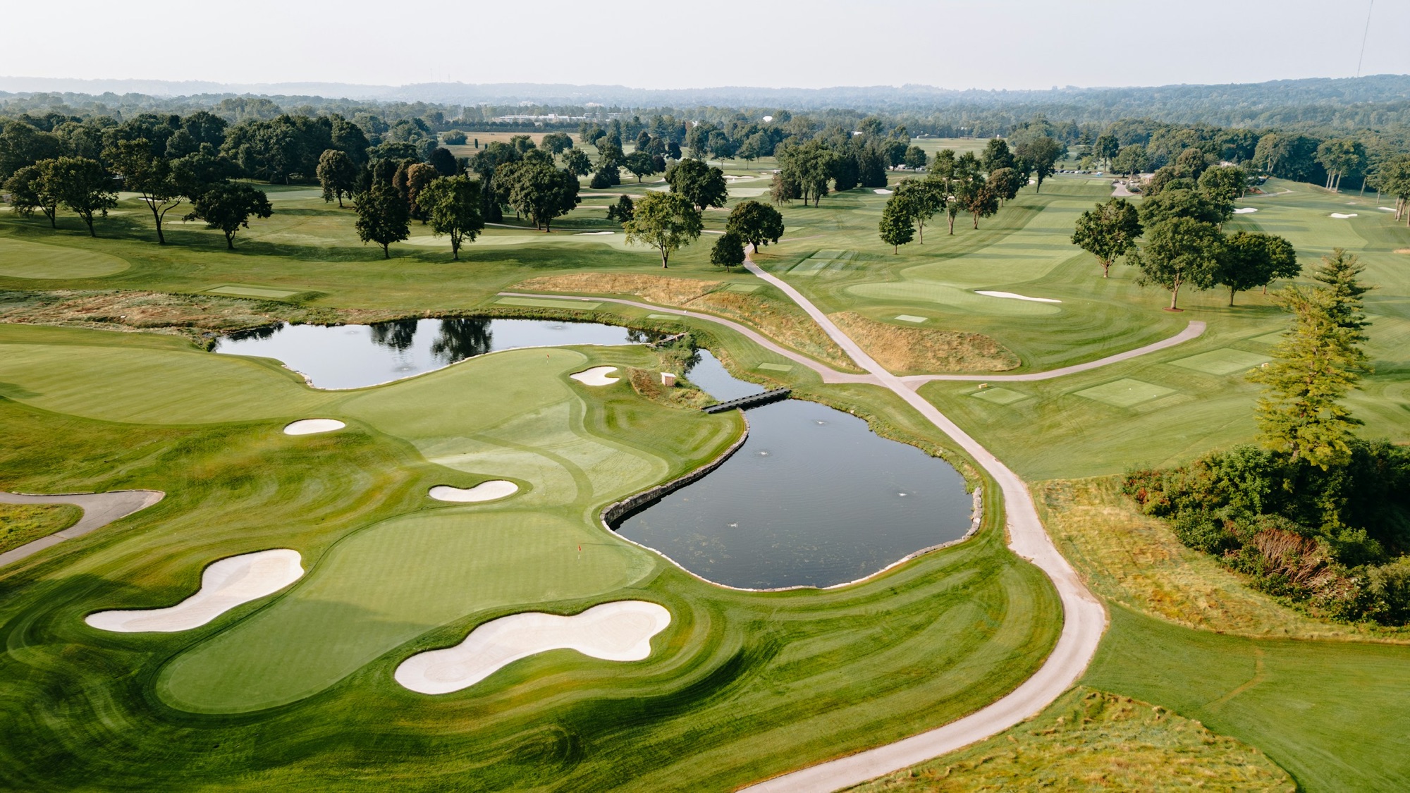 Aerial view of a lush championship golf course with manicured greens, sand bunkers, and water hazards framed by trees